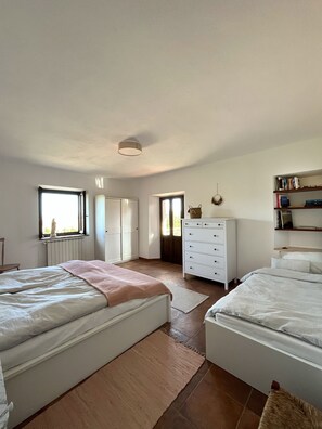 Quarto com duas camas, uma cômoda, uma estante e uma janela.