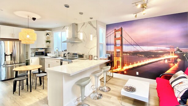 A modern kitchen with a central island, bar stools, and a large mural of the Golden Gate Bridge. - 5-bedroom whole apartment perfect for groups 1/2 block from San Francisco Border (Daly City)