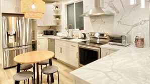 A modern kitchen with white cabinets, stainless steel appliances, a marble backsplash, and pendant lighting. - 5-bedroom whole apartment perfect for groups 1/2 block from San Francisco Border (Daly City)
