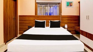 A hotel room with a large bed, wooden headboard, a window with bars, a wardrobe, and an air conditioning unit. - Collection O Sea Beach Puri (Brahmagiri)