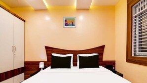 A bedroom with a bed, a nightstand, a lamp, a wardrobe, and a window with blinds. - Collection O Sea Beach Puri (Brahmagiri)
