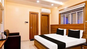 A bedroom with a wooden headboard, a bed with white and black bedding, a desk with a chair, and a window with blinds. - Collection O Sea Beach Puri (Brahmagiri)