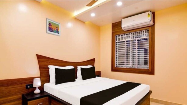 A neatly arranged bedroom with a bed, bedside table, lamp, and an air conditioning unit. - Collection O Sea Beach Puri (Brahmagiri)