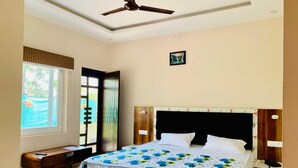 A bedroom with a bed, a desk, a chair, a ceiling fan, a window, and a door. - PHS KASAULI HILLS (Krishangarh)