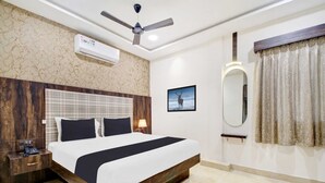 A modern hotel room with a large bed, a ceiling fan, an air conditioning unit, a bedside table with a phone, a nightstand, a wall-mounted mirror, and a framed picture. - Collection O Indiranagar (Bengaluru)