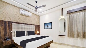 A modern hotel room with a large bed, a ceiling fan, an air conditioning unit, a nightstand, a bedside table, a lamp, a framed picture, a mirror, and a window with curtains. - Collection O Indiranagar (Bengaluru)
