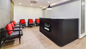 A reception area with a black reception desk, several red and black chairs, and a wooden floor. - Collection O Indiranagar (Bengaluru)
