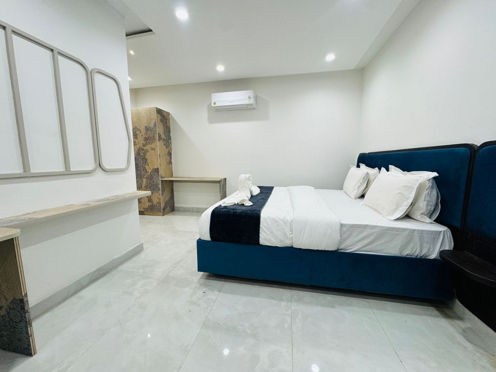 A modern hotel room with a large bed, a wooden accent wall, and a built-in bench.