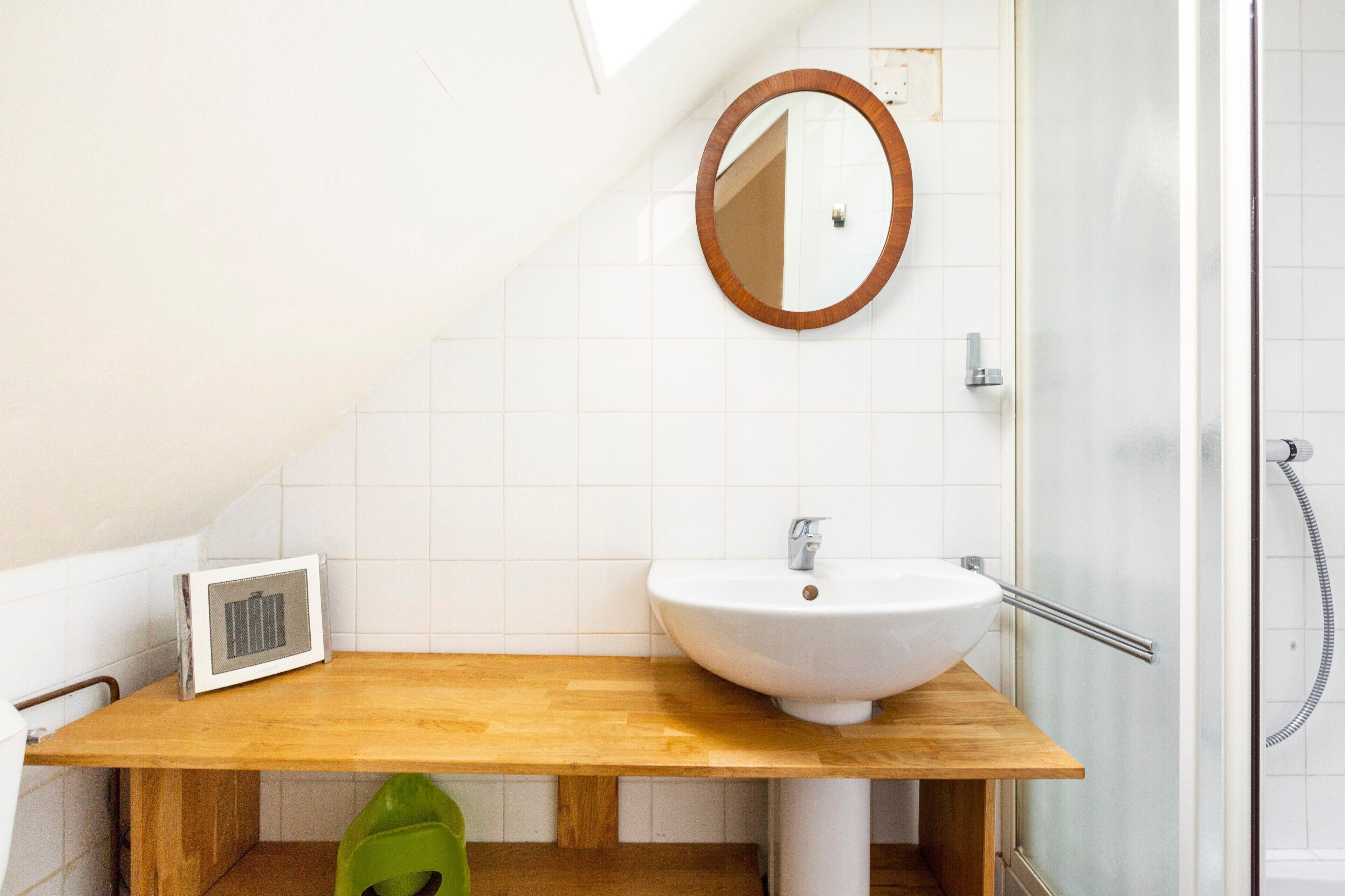 A bathroom with a wooden vanity, a white sink, a round mirror, and a glass shower enclosure.