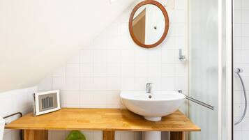 A bathroom with a wooden vanity, a white sink, a round mirror, and a glass shower enclosure.