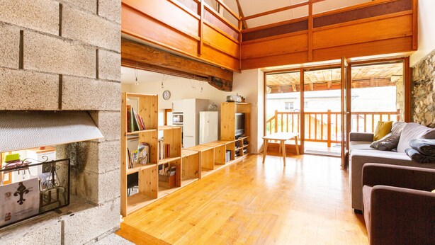 A spacious living area with a fireplace, wooden flooring, and a balcony with a stone wall.