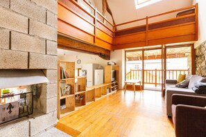 A spacious living area with a fireplace, wooden flooring, and a balcony with a stone wall. - Le gite à Géo – Charming Renovated House with Space, Authenticity, and Nature (Thoiry)