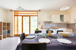 A dining area with a table set for four, a kitchen in the background, and a sliding glass door leading to an outdoor area.