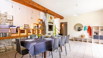A dining area with a stone wall, wooden beams, a fireplace, and a tiled floor.