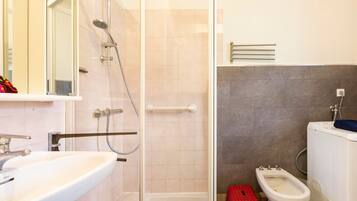 A bathroom with a shower, toilet, bidet, and sink.