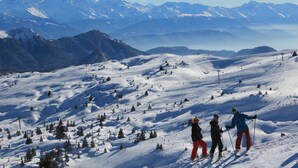 Un paysage de montagne enneigé, avec des skieurs, un ciel dégagé et des sommets lointains coiffés de neige.