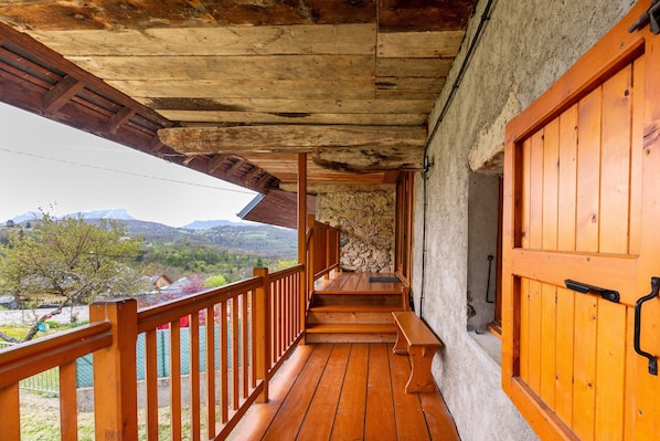 A wooden balcony with a stone wall, wooden steps, and a wooden door.