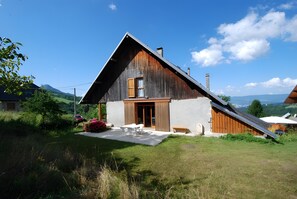 A rustic wooden house with a sloped roof, a front porch, and a paved driveway.
