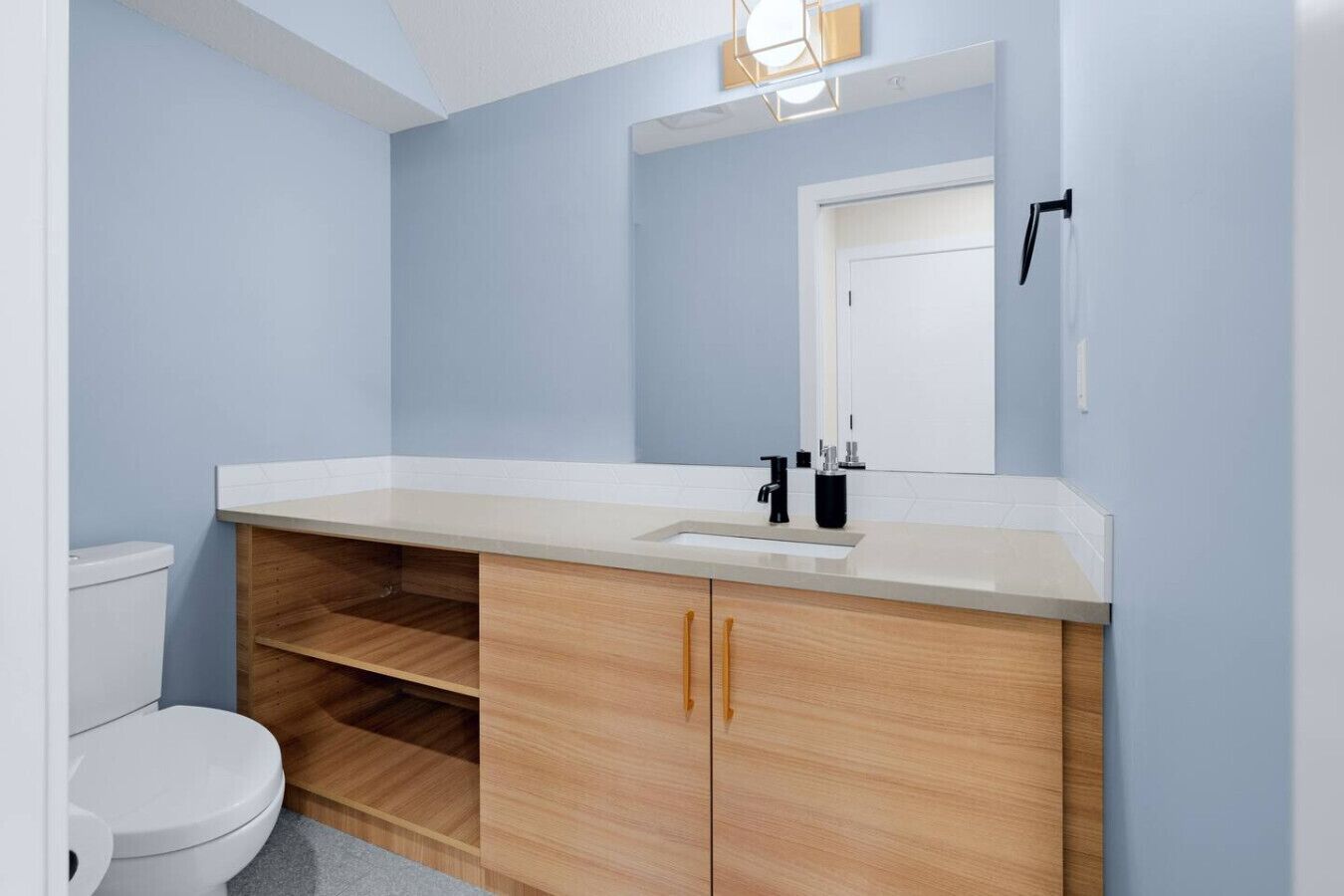 Un baño con inodoro blanco, tocador de madera con lavabo y espejo.