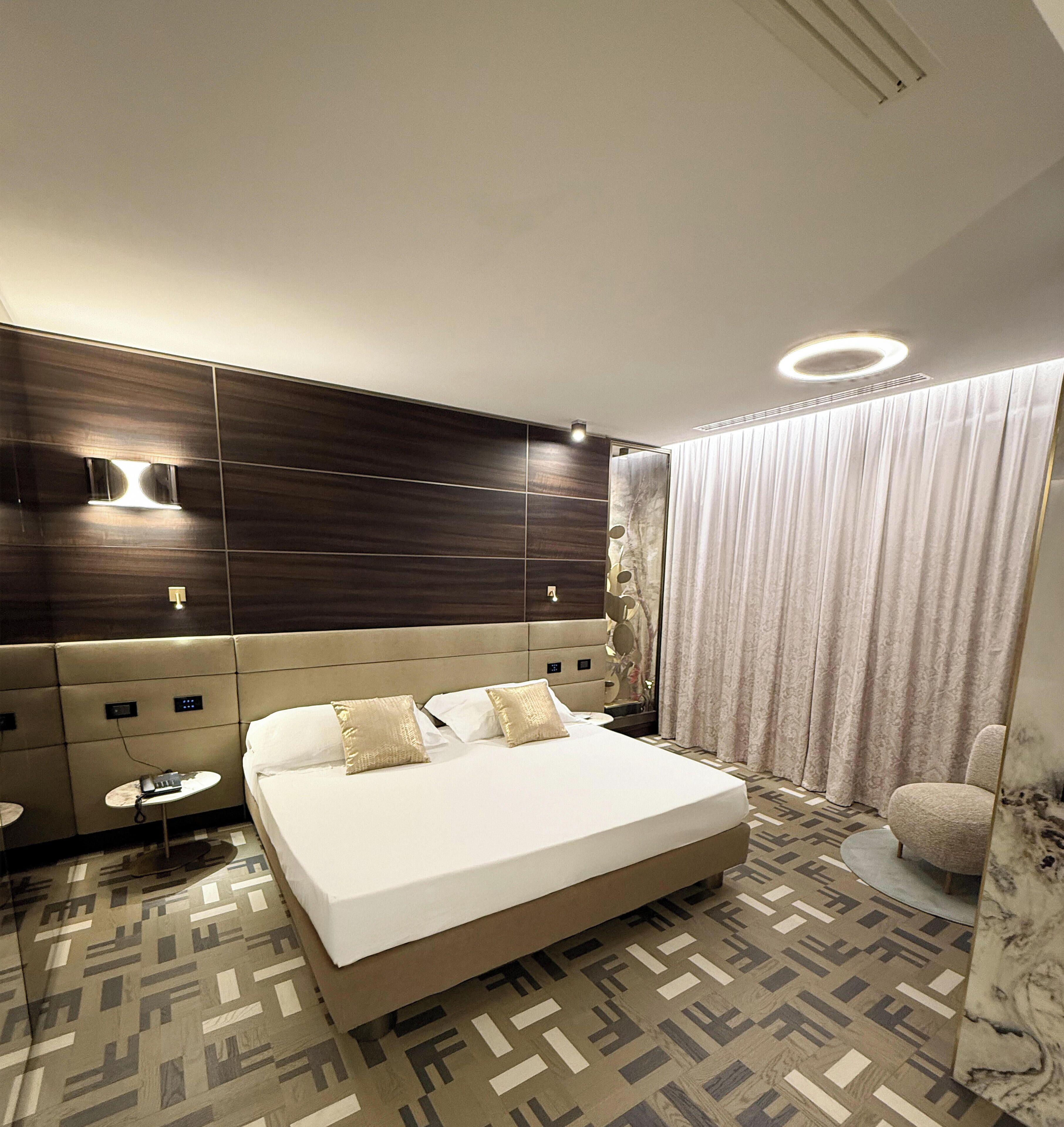Une chambre d’hôtel moderne dotée d’un grand lit, d’une table de chevet, d’un miroir et d’un coin salon avec un fauteuil.