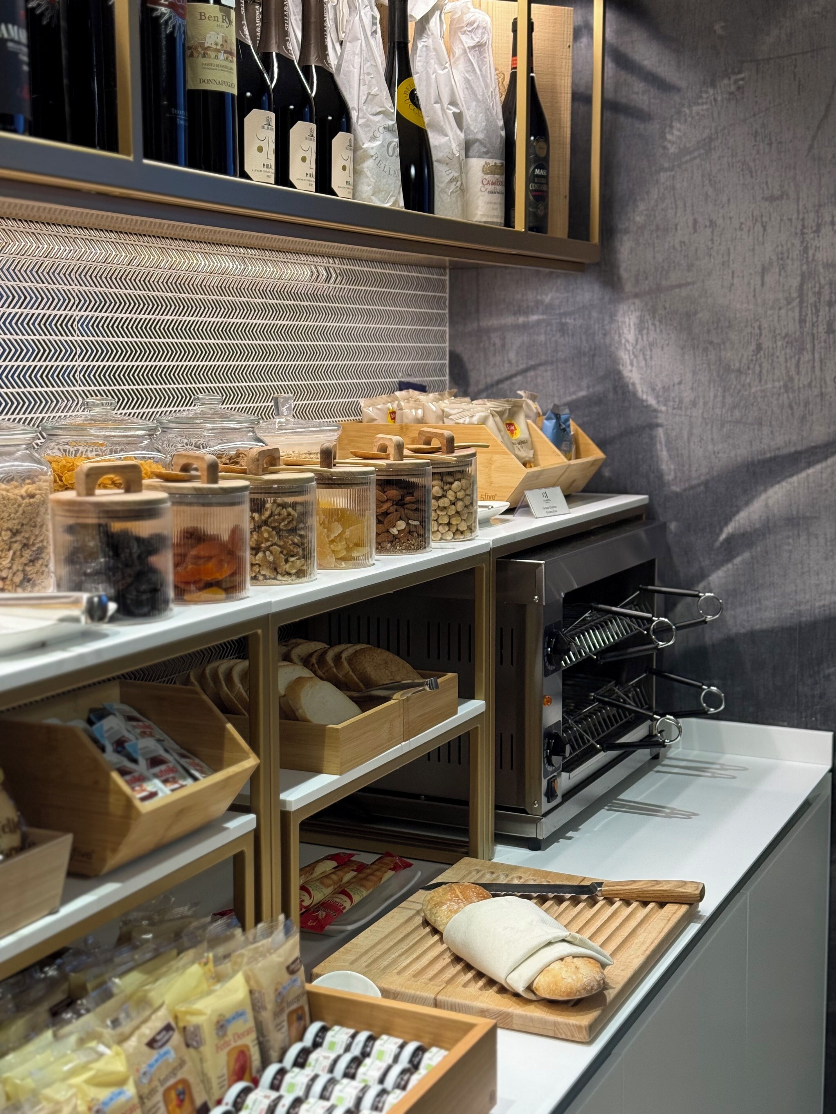 Mostrador de panadería con panes, pasteles y una estantería para vinos.