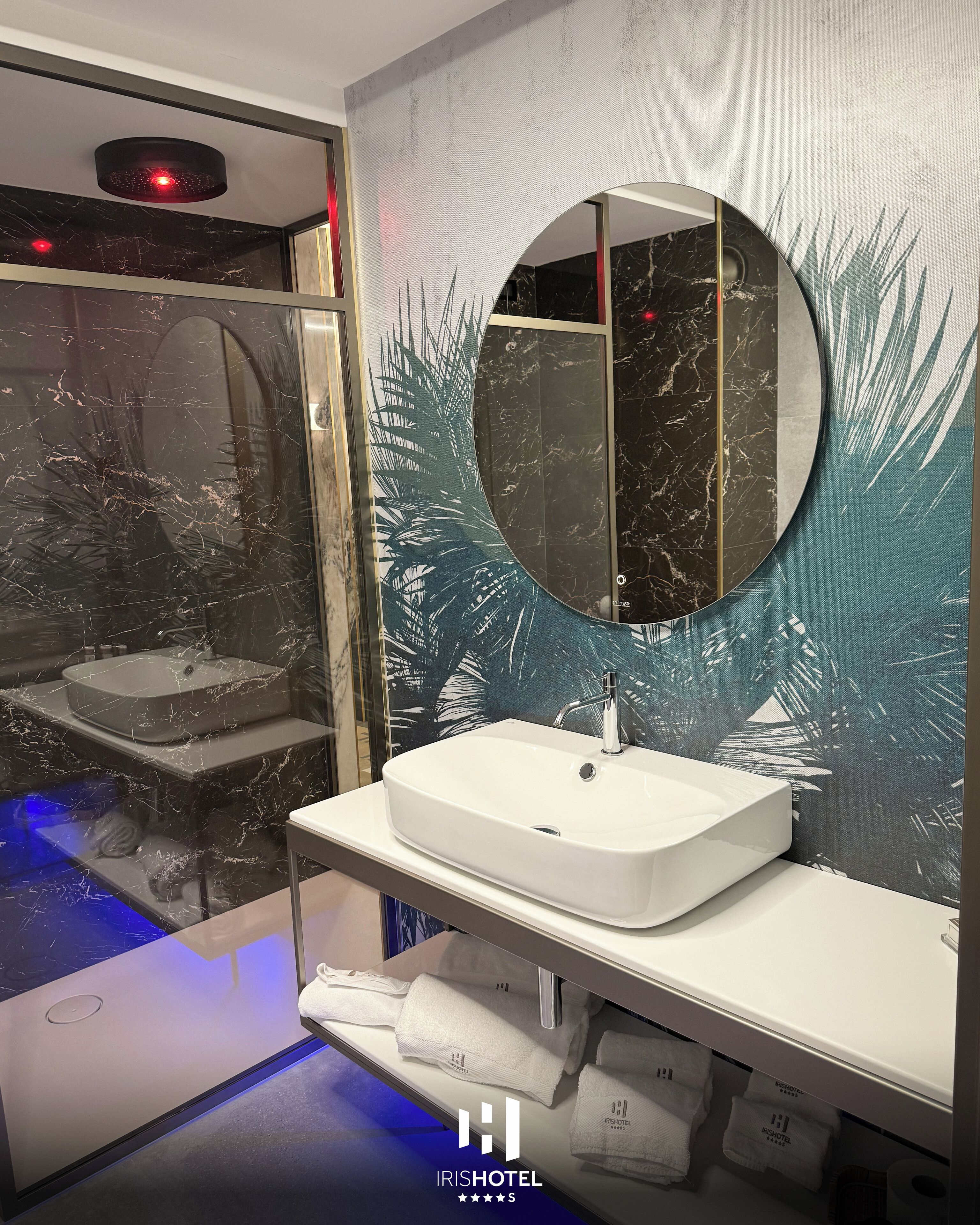 A modern bathroom with a marble sink, a round mirror, and a shower area with a glass door.