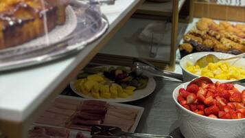 A buffet with various food items under glass domes, including pastries, fruits, and meats.
