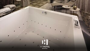 Una habitación de hotel moderna con una bañera grande, un sofá, un televisor y una chimenea.