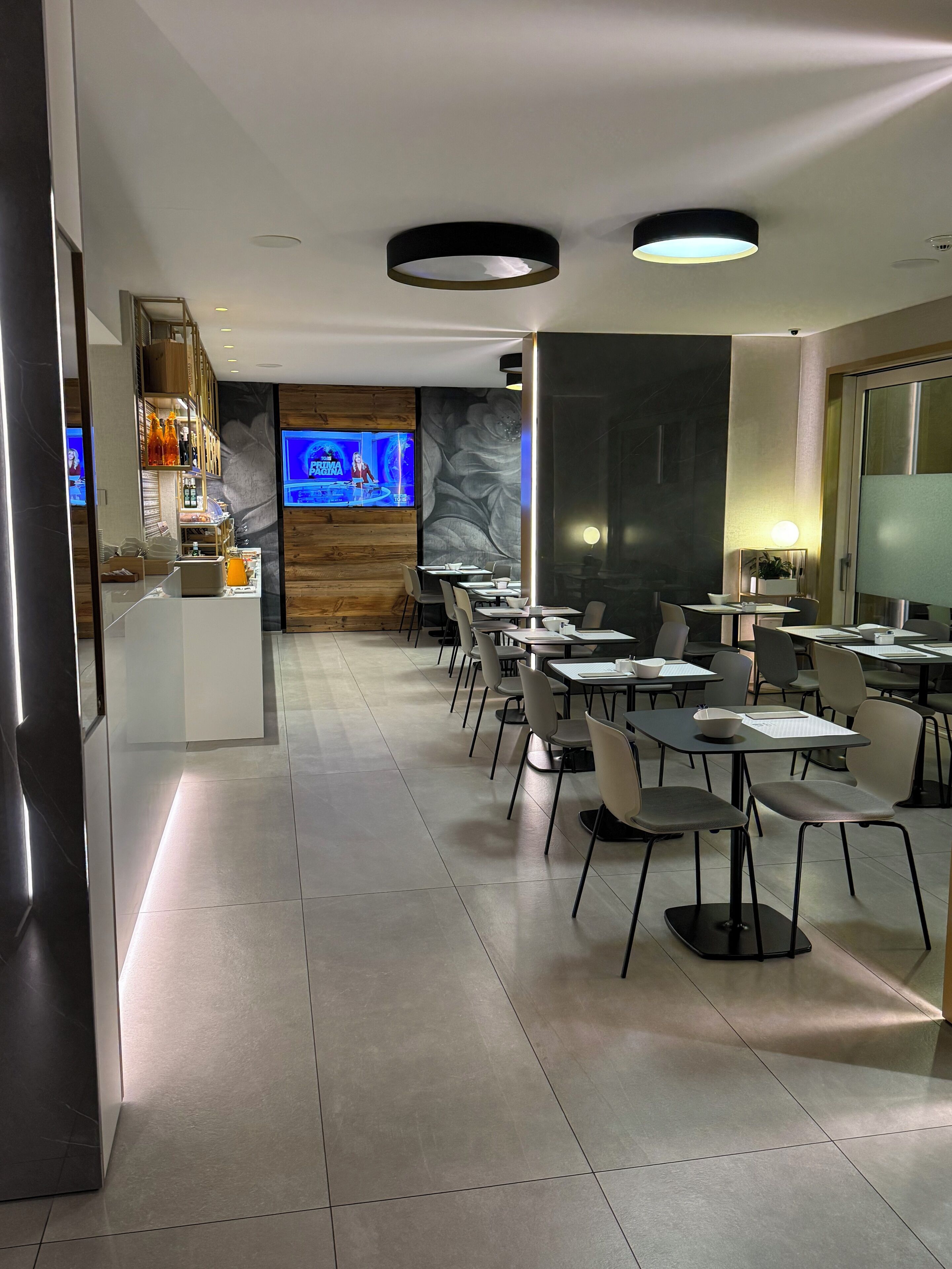 A modern restaurant with a long counter, multiple tables, and a TV screen displaying a news program.