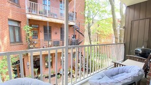 A balcony with two cushioned chairs, a grill, and a view of a brick building with multiple windows and balconies. - 2-bedroom large impeccable apartment in fabulous Montréal. (Montréal)