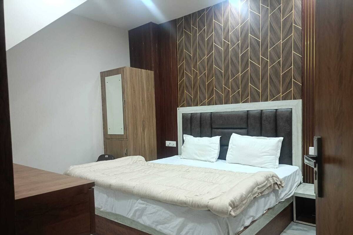A bedroom with a bed, a wooden wardrobe, a mirror, and a wall with a geometric pattern.