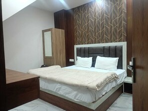 A bedroom with a bed, a wooden wardrobe, a mirror, and a wall with a geometric pattern. - Hotel Jay Palace (Agra)