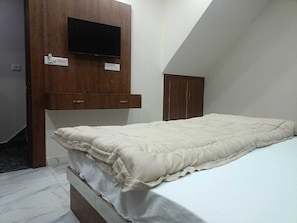 A bedroom with a bed, a TV mounted on a wooden cabinet, and a wardrobe. - Hotel Jay Palace (Agra)