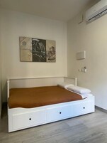 Un dormitorio con una cama blanca, una manta marrón y un aire acondicionado instalado en la pared.