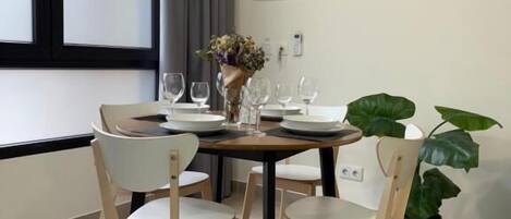 A dining area with a round table, four chairs, a vase with flowers, and a potted plant.