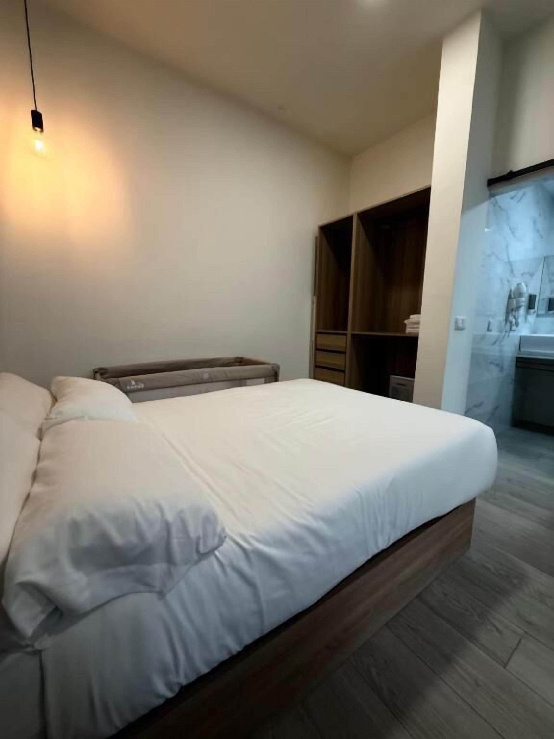 A modern bedroom with a large bed, wooden headboard, built-in wardrobe, and a small bedside table.