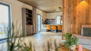 A modern living room with a wooden ceiling, a dining area with a table and chairs, and a sofa with a plant and candle on a wooden table. - Stylish chalet at lake Afritzer See with sauna (Afritz am See)