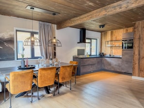 Uma cozinha moderna com armários de madeira, forno embutido e um espaço de refeições com mesa e cadeiras.
