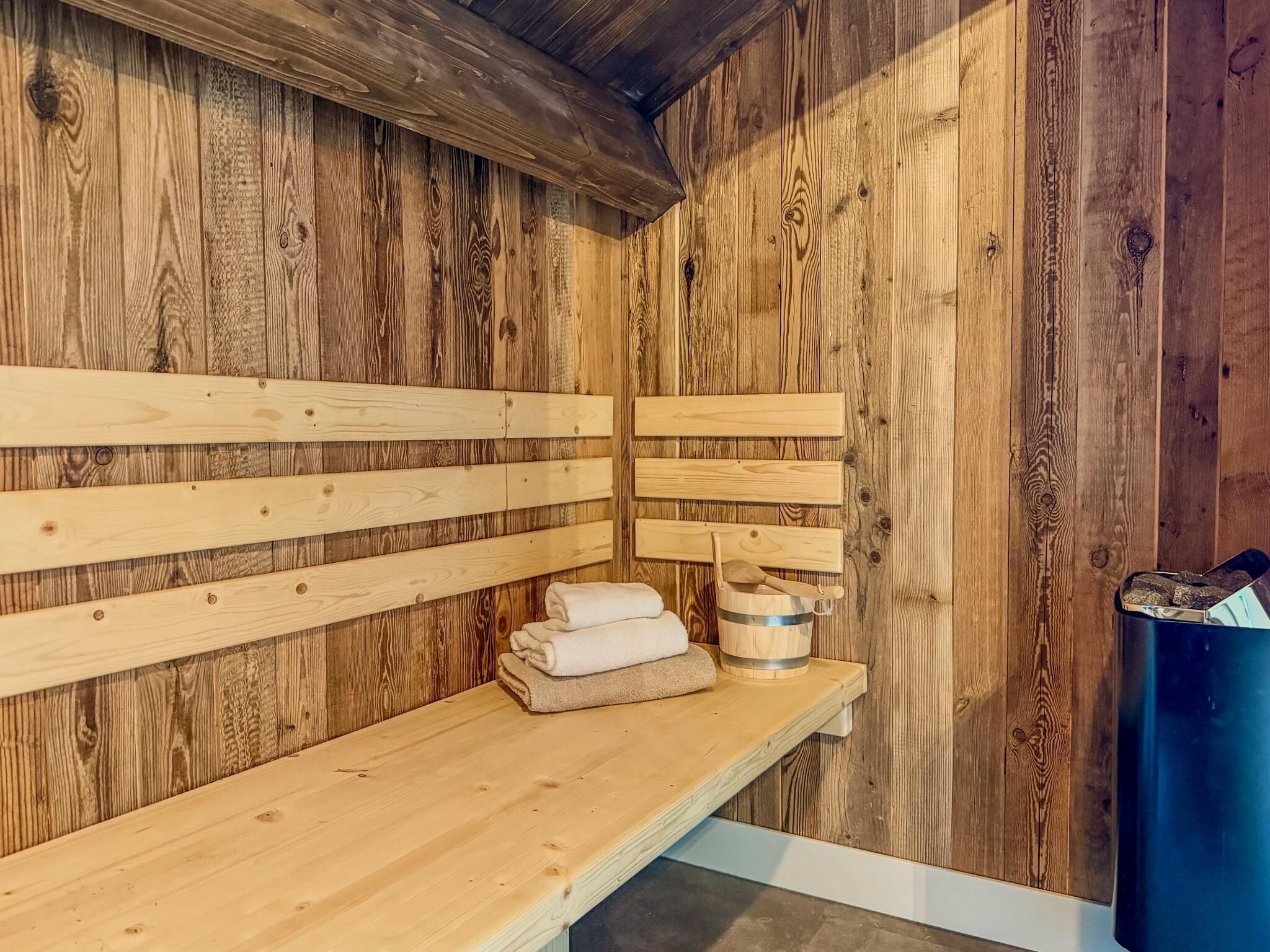 Un sauna avec des bancs en bois, un banc avec des serviettes et un seau avec une louche en bois.