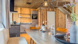 A cozy kitchen with wooden walls, a dining table with glasses and a bottle, and a modern pendant light. - Stylish chalet at lake Afritzer See with sauna (Afritz am See)