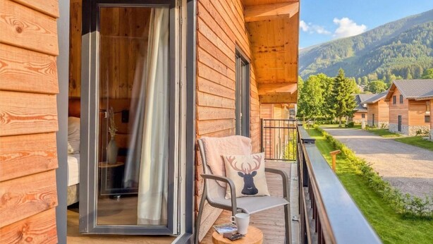 A wooden cabin with a balcony, a chair with a cushion, and a view of a mountain landscape. - Stylish chalet at lake Afritzer See with sauna (Afritz am See)