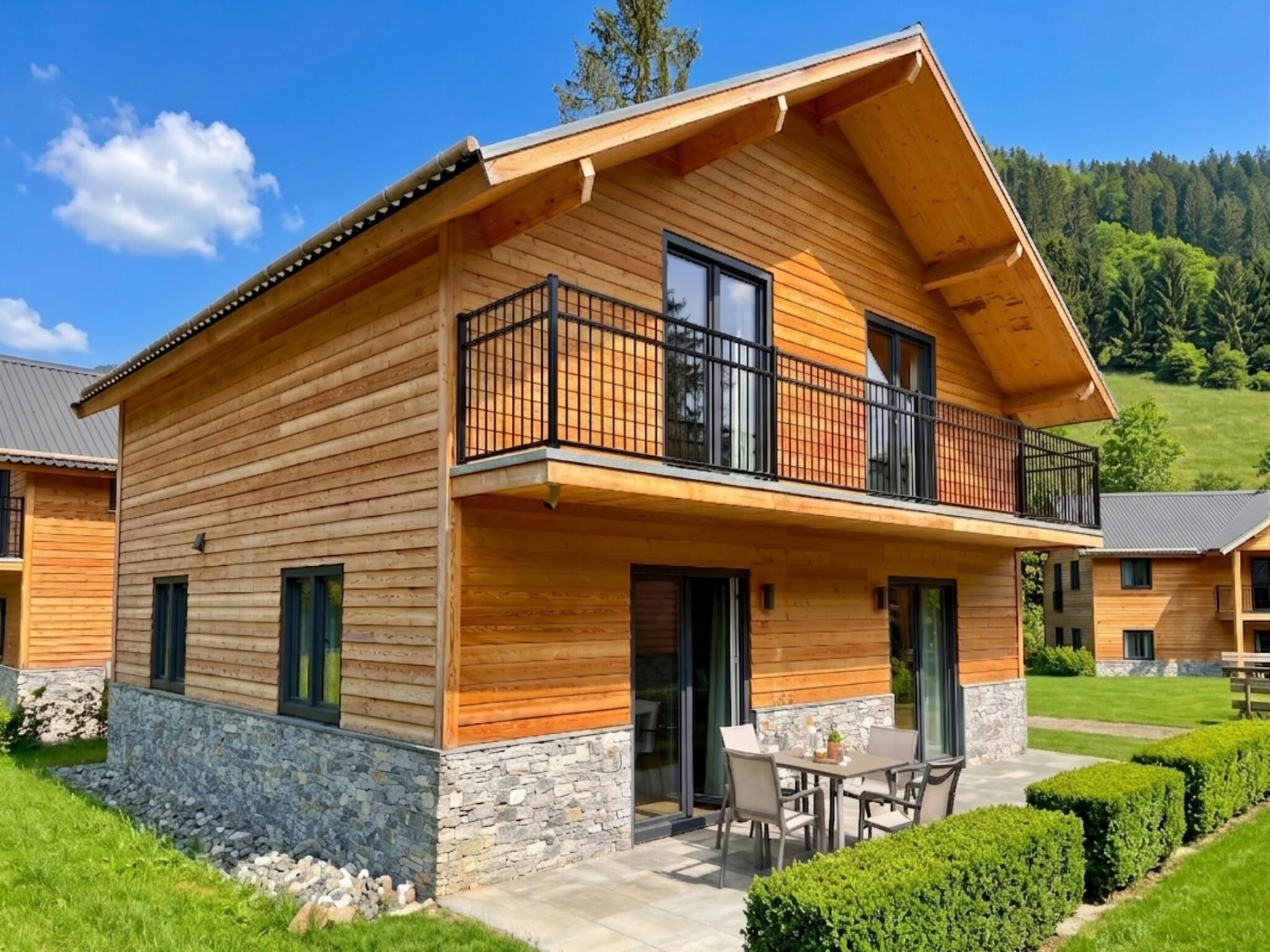 Una casa de madera de dos pisos con balcón, base de piedra y un patio con mobiliario exterior.