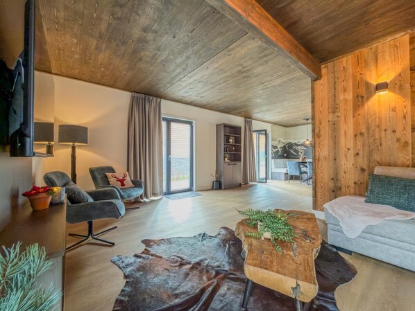 Une pièce spacieuse avec un plafond en bois, un canapé, une table basse, une bibliothèque et un coin repas avec des chaises.