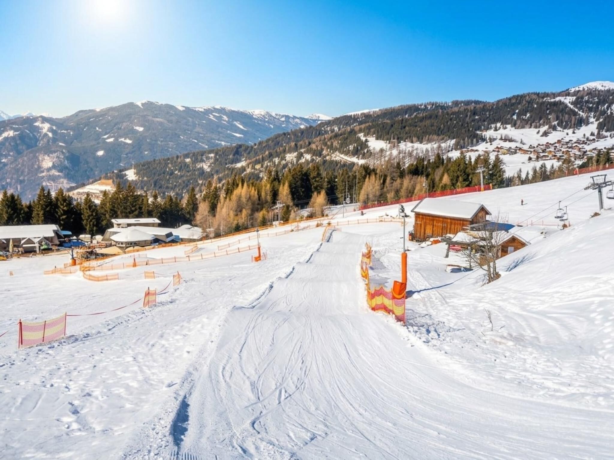 A snowy ski slope with a ski lift and buildings in the background.