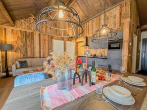 A wooden interior with a dining table set for two, a sofa, and a kitchen area. - Stylish apartment with mountain and lake views (Afritz am See)