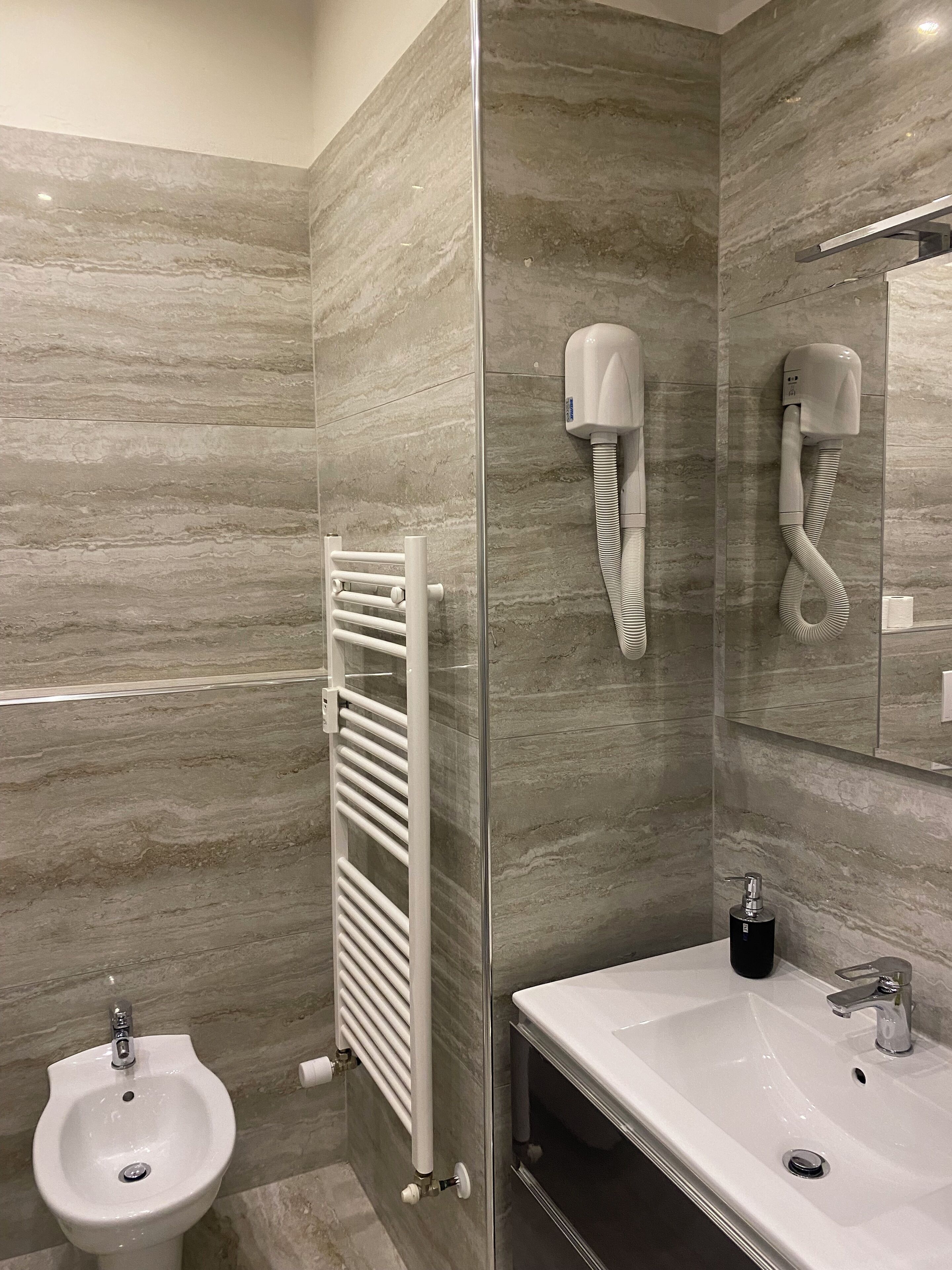 Ein Badezimmer mit Bidet, Handtuchhalter, Waschbecken und zwei an der Wand befestigten Haartrocknern.