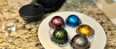 Une machine à café Nespresso posée sur un plan de travail de cuisine, avec une assiette remplie de capsules de café aux couleurs vives.