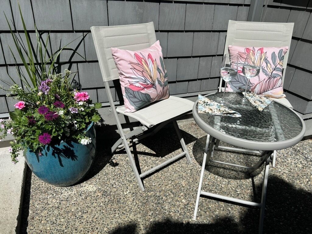 Dos sillas con cojines estampados, una mesa redonda y una planta en maceta con flores.
