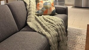 A modern living room with a grey sofa, a patterned throw blanket, and a colorful pillow. - Fern Hollow - unwind in this nature inspired suite in Edgemont Village. (North Vancouver)