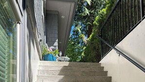 A staircase leading to a second-floor landing, surrounded by greenery and a large blue planter with flowers. - Fern Hollow - unwind in this nature inspired suite in Edgemont Village. (North Vancouver)